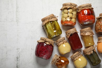Photo of Many jars with different preserved products on white table, flat lay. Space for text