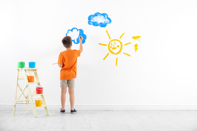 Photo of Little child painting cloud on white wall in room