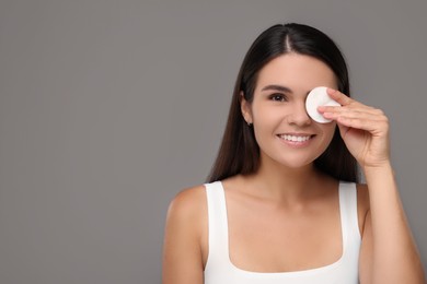 Photo of Young woman cleaning her face with cotton pad on grey background. Space for text