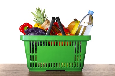 Photo of Shopping basket with grocery products on wooden table against white background