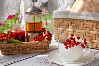 Photo of Cup of hot drink and viburnum berries on white wooden table indoors