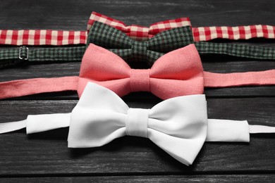 Photo of Stylish color bow ties on black wooden table, closeup
