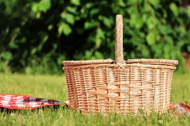 Picnic basket with checkered tablecloth on green grass outdoors, space for text