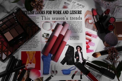 Bright lip glosses among different cosmetic products and fashion magazine on table, flat lay