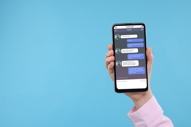 Image of Woman texting with friend using messaging application on smartphone against light blue background, closeup. Space for text