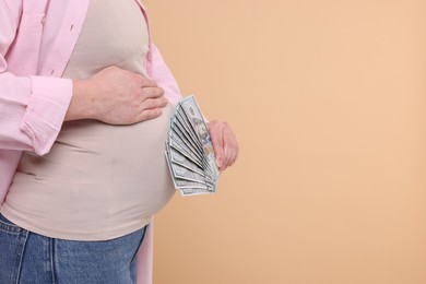 Photo of Surrogate mother. Pregnant woman with dollar banknotes on beige background, closeup. Space for text