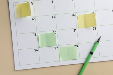 Photo of Timetable. Calendar page with sticky notes and pen on beige background, top view