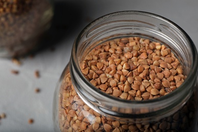 Photo of Uncooked buckwheat in glass jar on table, closeup