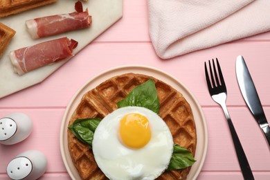 Photo of Fresh Belgian waffles with fried egg, basil and jamon served for breakfast on pink wooden table, flat lay
