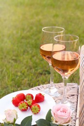 Photo of Picnic basket with glassesdelicious rose wine, strawberries and flowers outdoors