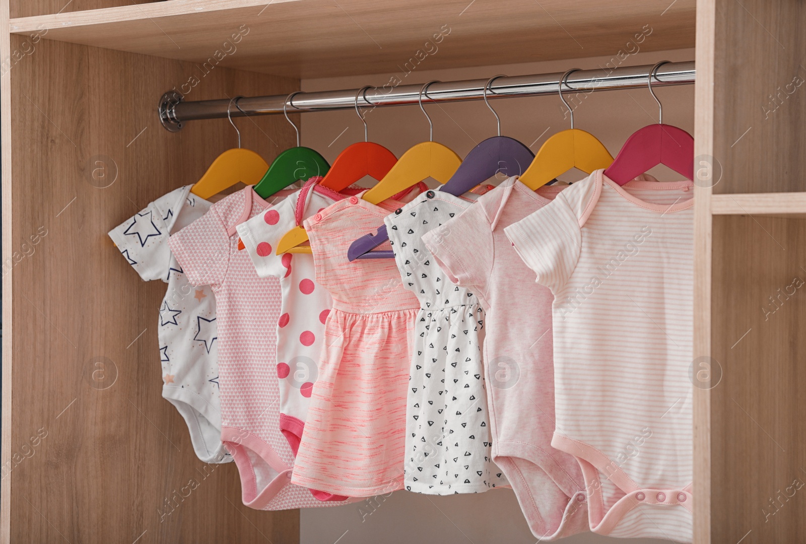 Photo of Hangers with baby clothes on rack in wardrobe