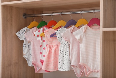 Photo of Hangers with baby clothes on rack in wardrobe