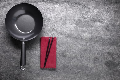 Photo of Empty wok and chopsticks on grey table, flat lay. Space for text