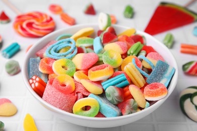 Photo of Bowl of tasty colorful jelly candies on white tiled table, closeup