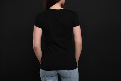 Photo of Woman wearing black t-shirt on dark background, back view