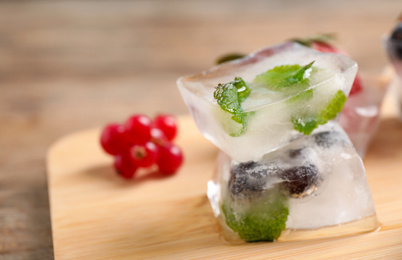 Photo of Ice cubes with different berries and mint on wooden board, closeup