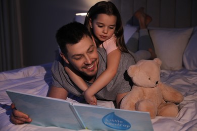 Photo of Father with his daughter reading book in bed at home