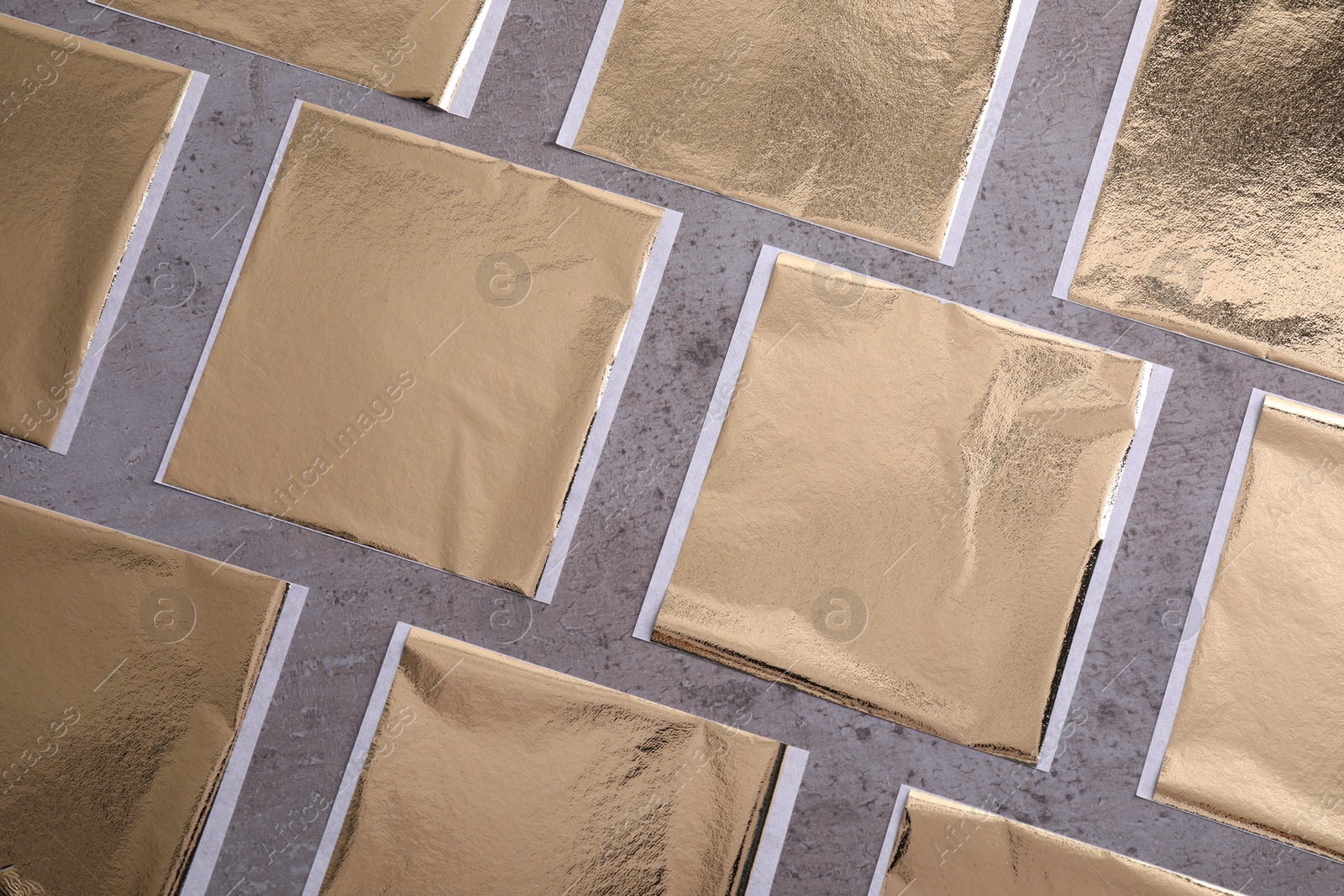 Many edible gold leaf sheets on grey textured table, flat lay Photo of Many edible gold leaf sheets on grey textured table, flat lay