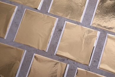 Photo of Many edible gold leaf sheets on grey textured table, flat lay