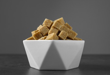 Photo of Brown sugar cubes in bowl on grey table