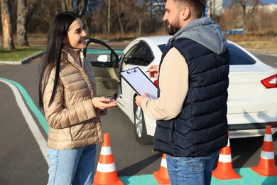 Photo of Young woman with instructor near car at driving school test track