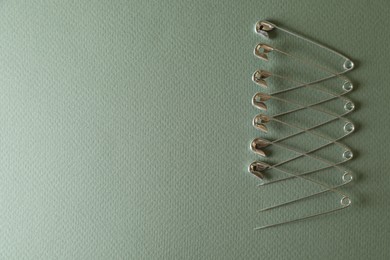 Photo of Many safety pins on green background, flat lay. Space for text