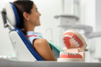 Photo of Jaws model at table in modern dentist's office and blurred woman on background. Space for text