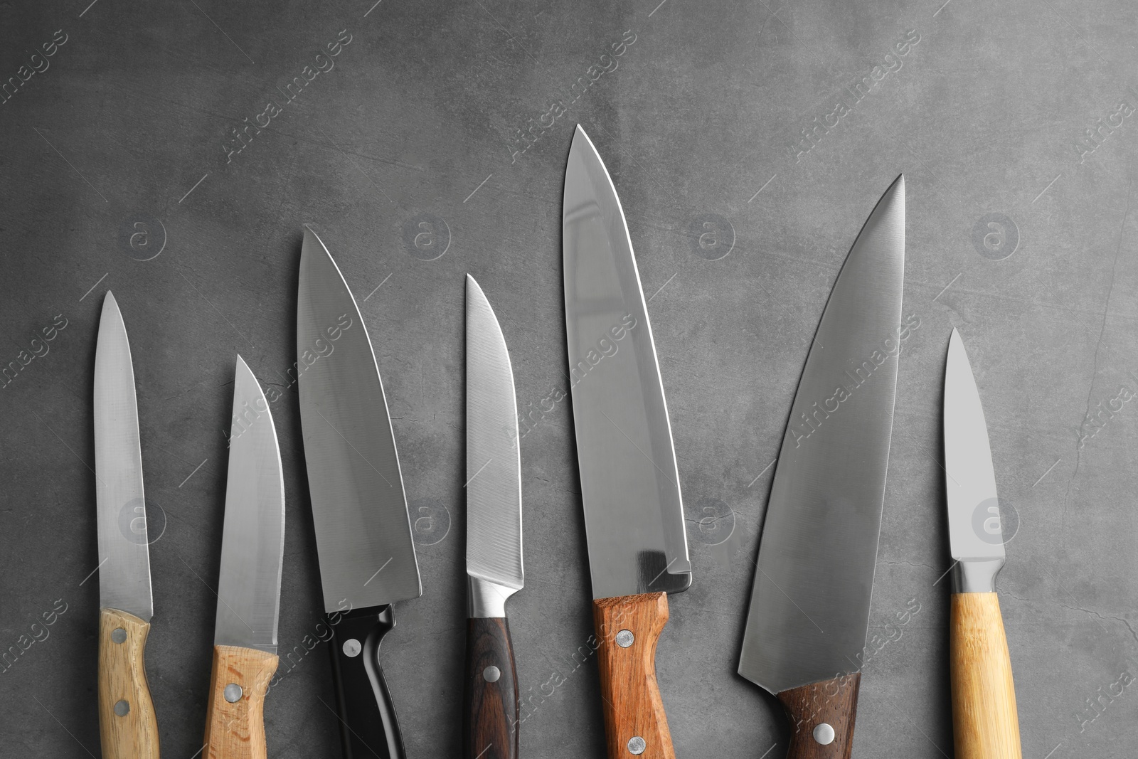 Photo of Many different knives on grey textured table, flat lay