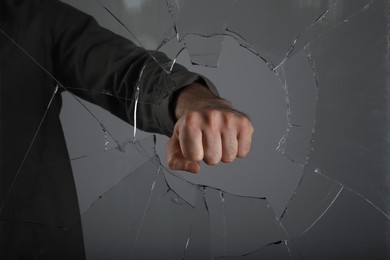 Photo of Man breaking window with fist on grey background, closeup