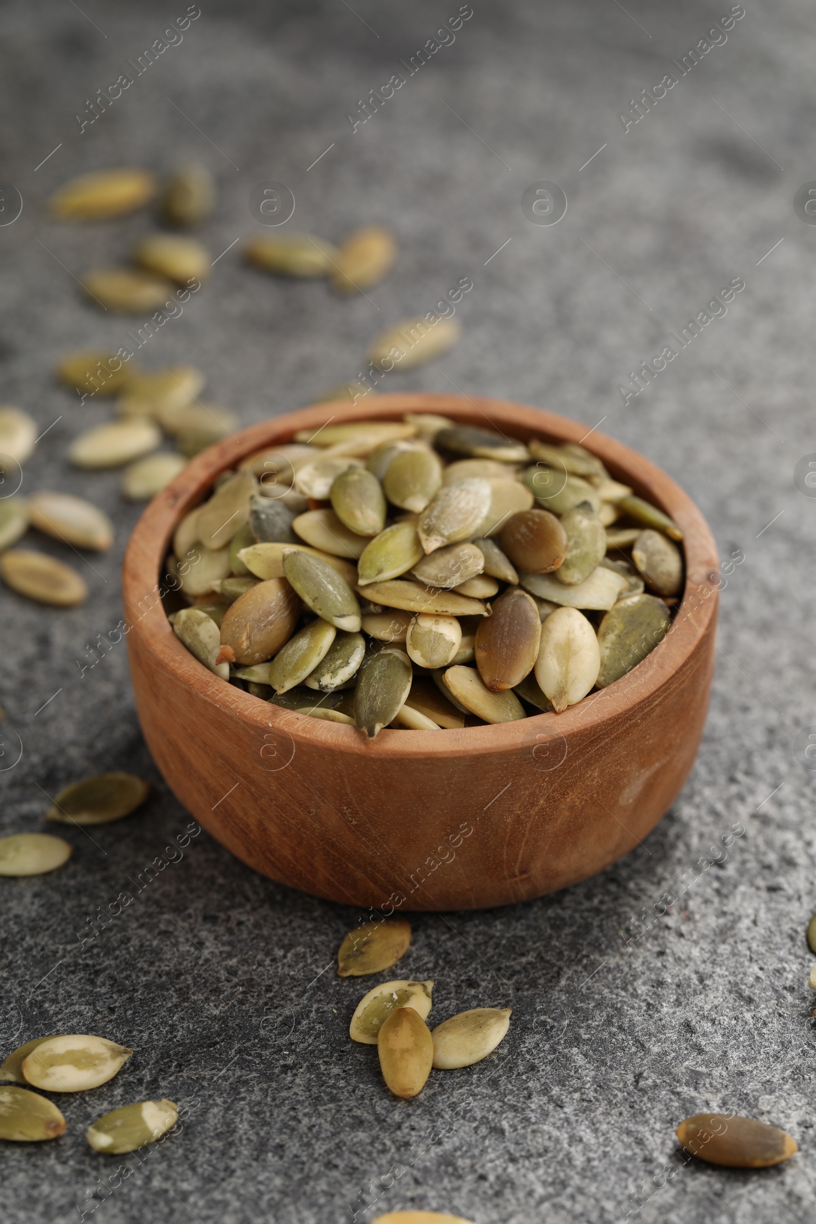 Photo of Wooden bowl with peeled pumpkin seeds on grey table
