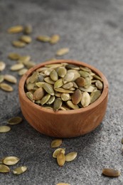 Wooden bowl with peeled pumpkin seeds on grey table