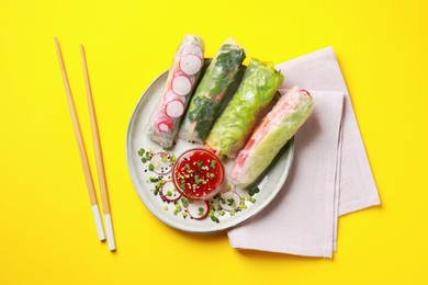 Photo of Delicious spring rolls served with sauce on yellow background, flat lay