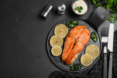 Photo of Delicious roasted fish served on black table, flat lay. Space for text