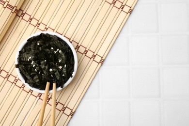 Chopped nori sheets, chopsticks and bamboo mat on white table, flat lay. Space for text
