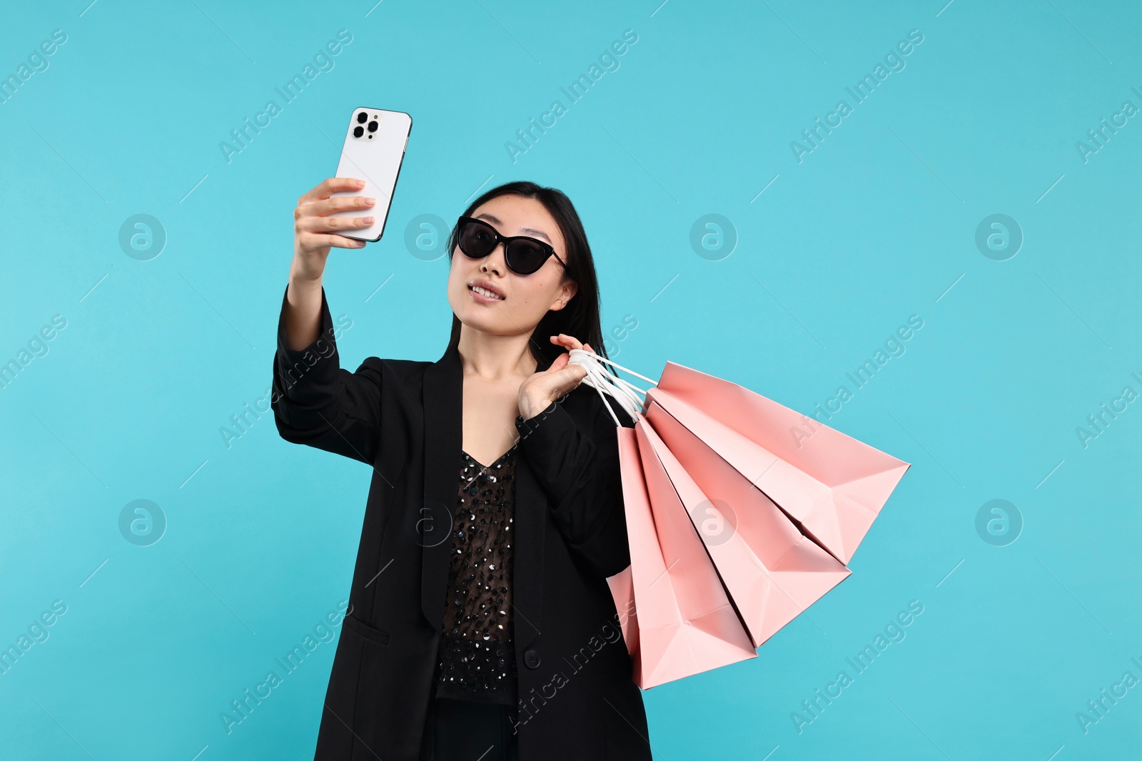 Photo of Smiling woman with shopping bags taking selfie on light blue background