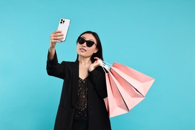 Photo of Smiling woman with shopping bags taking selfie on light blue background