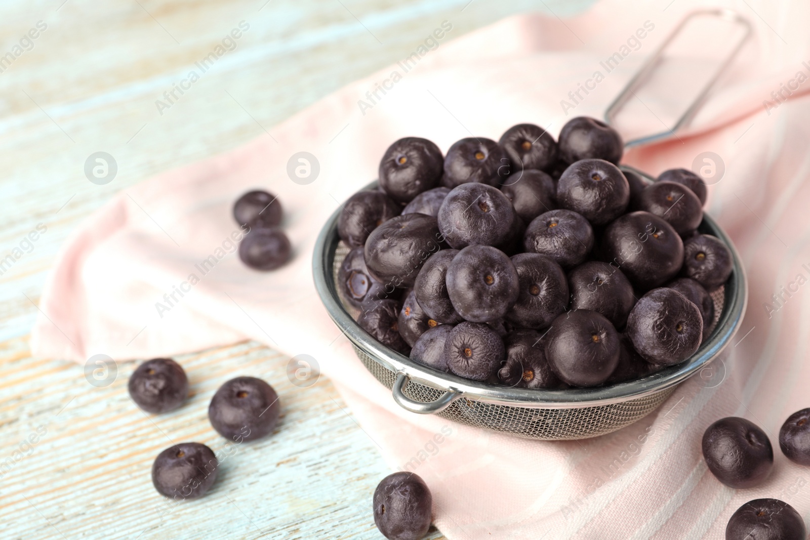 Photo of Metal sieve of fresh acai berries on light wooden table, closeup. Space for text