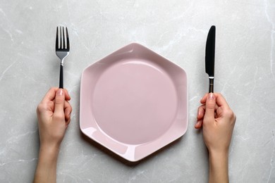 Photo of Woman with fork, knife and empty plate at light grey table, top view