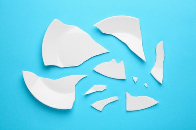 Photo of Pieces of broken ceramic plate on light blue background, flat lay