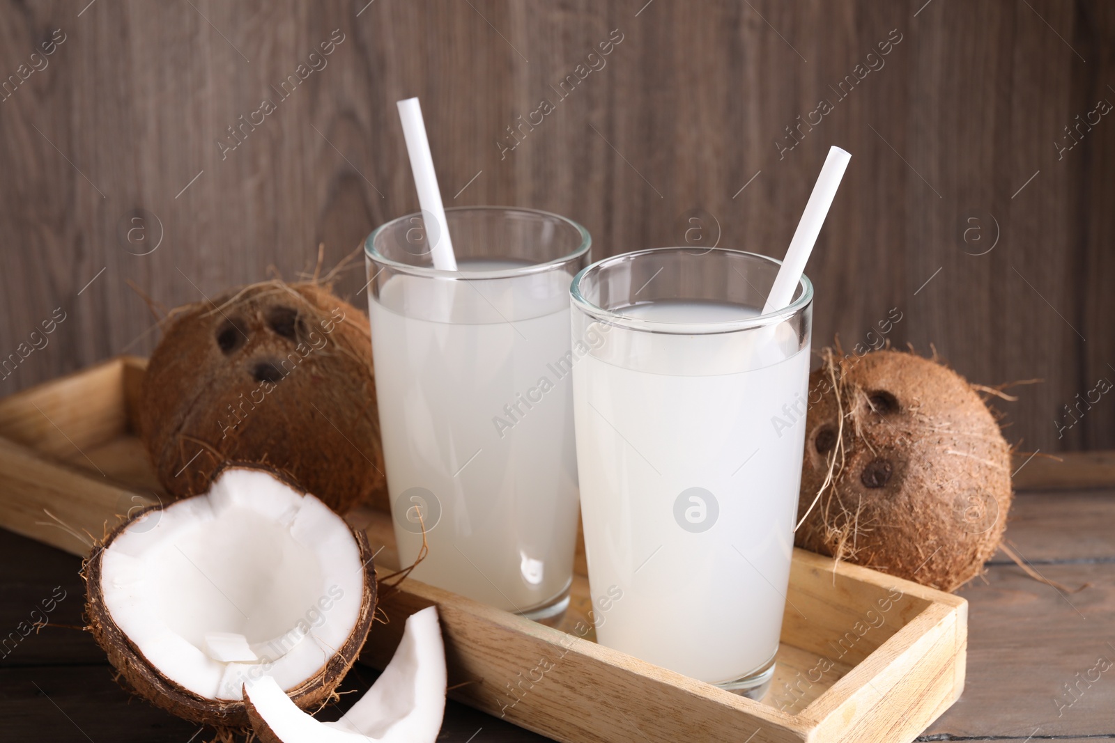 Photo of Glasses of coconut water with straws and nuts on wooden table