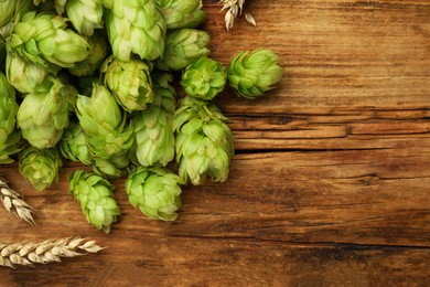 Photo of Heap of fresh green hops and wheat ears on wooden table, flat lay. Space for text