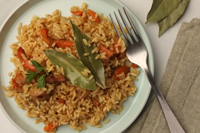 Photo of Delicious pilaf, bay leaves and fork on white table, flat lay