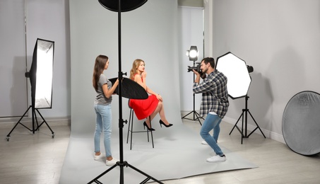 Photo of Professional photographer with assistant taking picture of young woman in modern studio