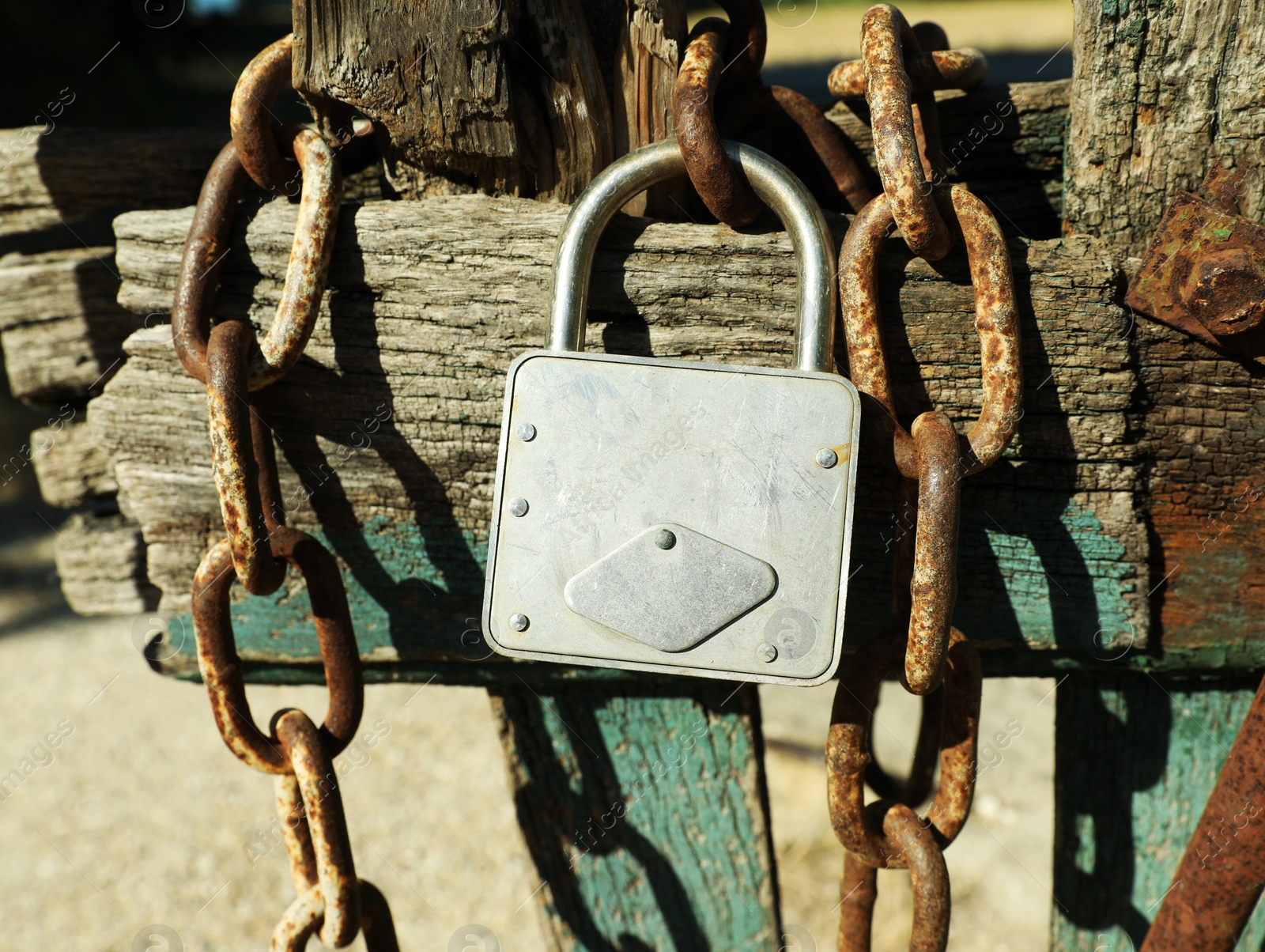 Photo of Old wooden fence with metal chain and lock on sunny day, closeup