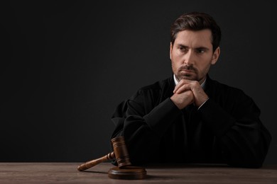 Photo of Judge with gavel sitting at wooden table against black background. Space for text