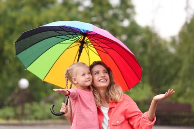 Photo of Happy mother and daughter with bright umbrella under rain outdoors