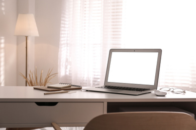 Photo of Laptop on desk near window in office. Comfortable workplace