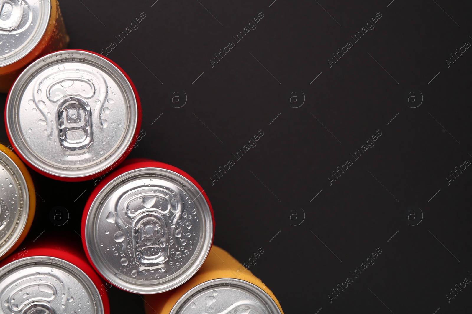 Photo of Energy drinks in wet cans on dark background, top view. Space for text