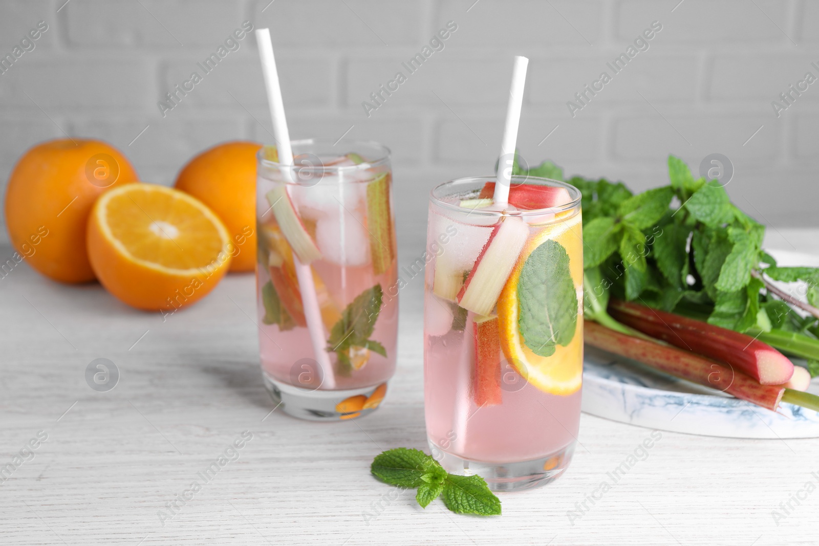 Photo of Tasty rhubarb cocktail with orange on white wooden table