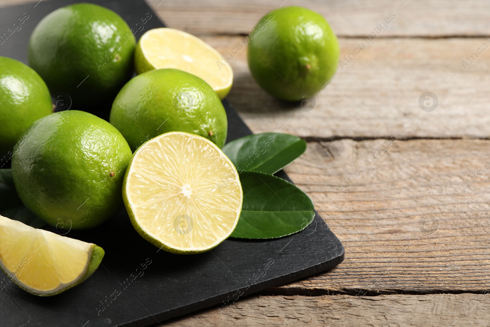 Photo of Fresh limes and green leaves on wooden table. Space for text